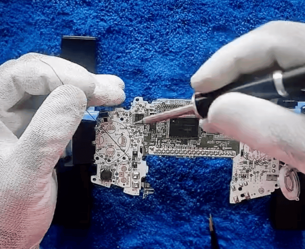 RetroGear-moddingtechnicus die een Nintendo Game Boy Advance-moederbord soldeert terwijl hij witte handschoenen draagt.